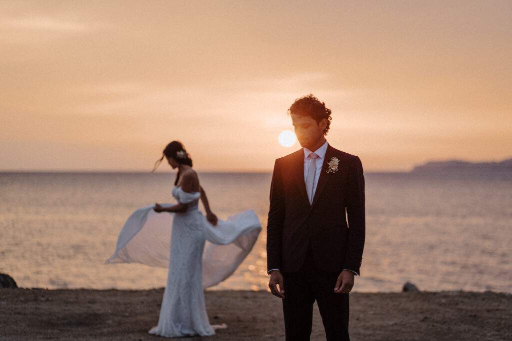 Sposi al tramonto sul mare, il velo della sposa mosso dal vento – golden hour