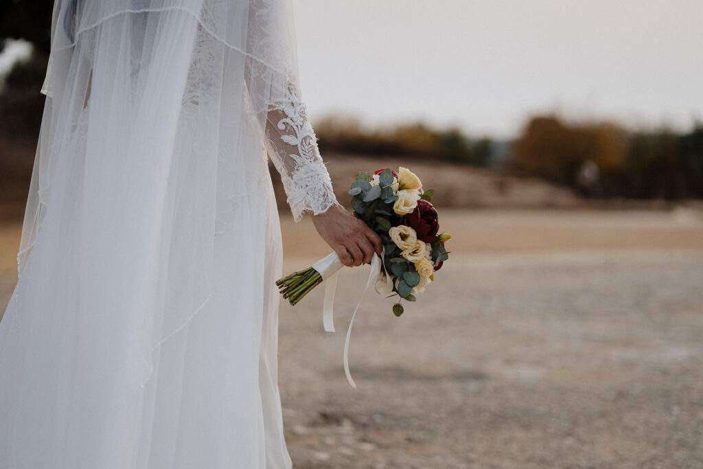 Sposa con il velo e il bouquet in mano su una strada sterrata
