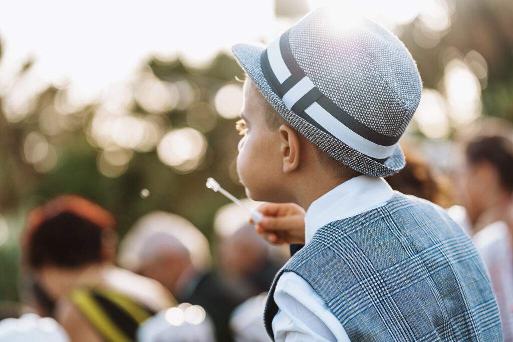Un bambino con il cappello soffia bolle di sapone durante un matrimonio in Sicilia