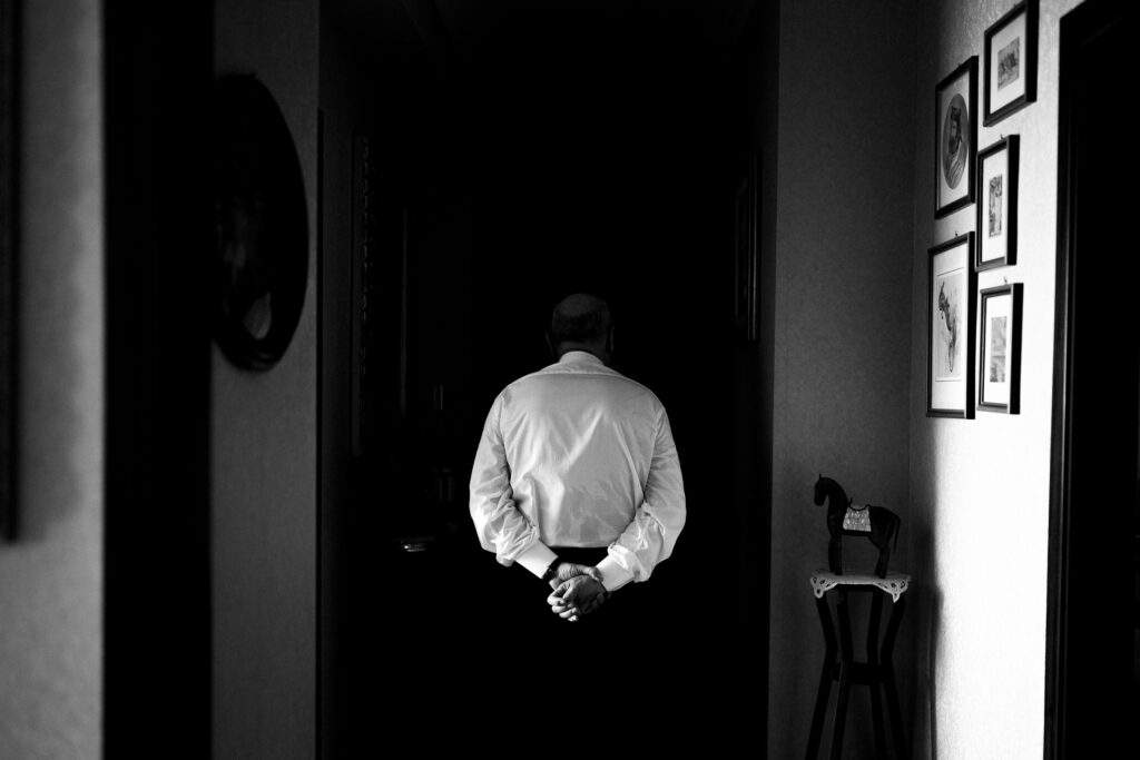 Un uomo di spalle con le mani dietro la schiena in un corridoio buio, foto di reportage in bianco e nero