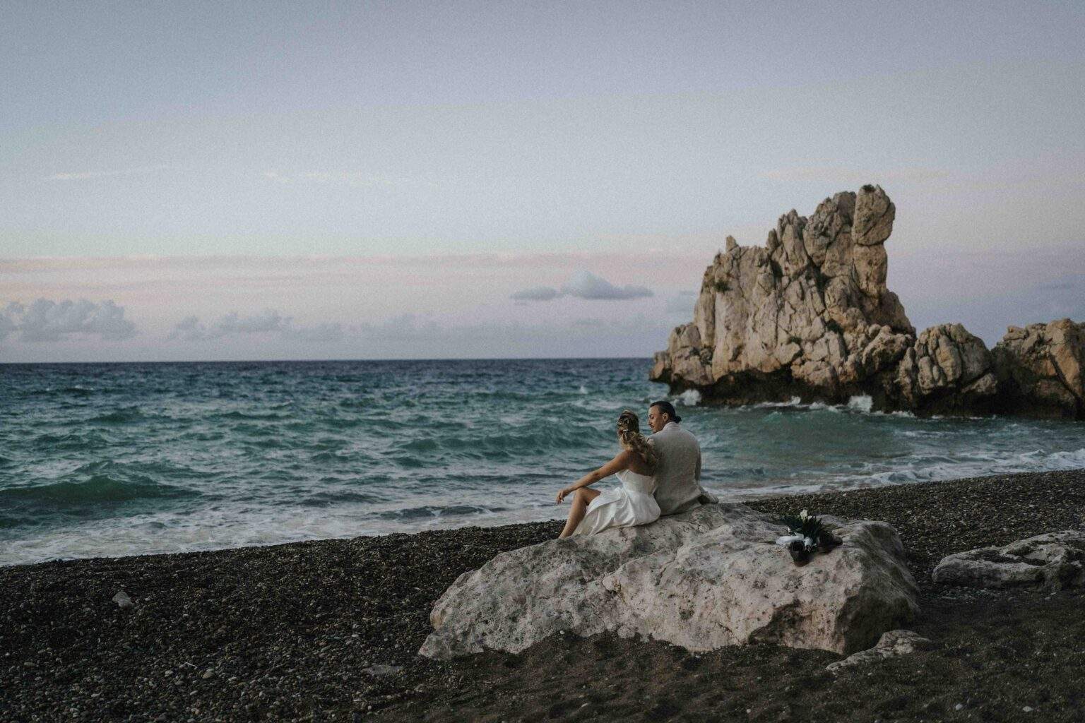 Carla e Giorgio seduti su uno scoglio in riva al mare al tramonto – matrimonio sul mare in Sicilia