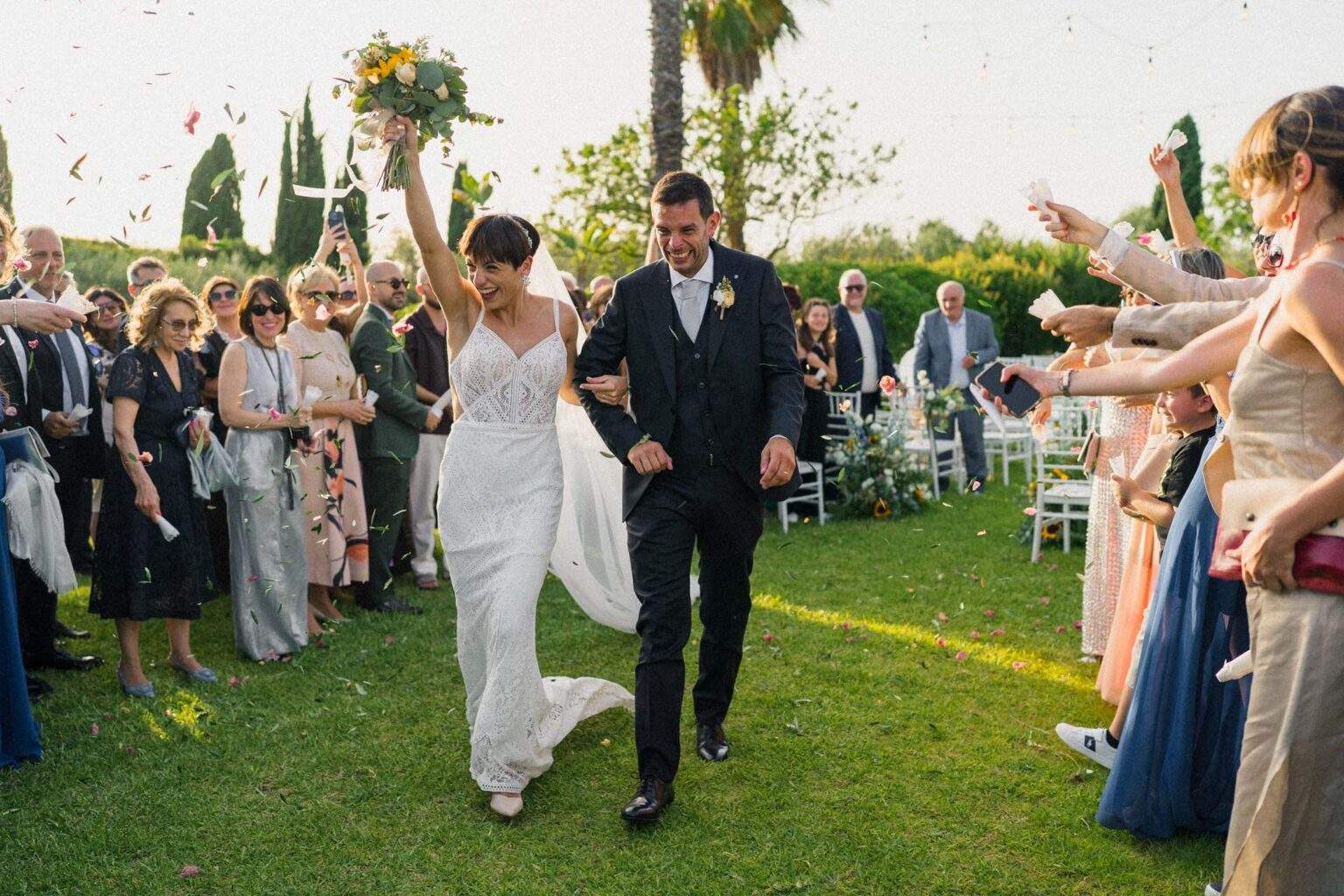 Lia e Giorgio escono tra gli invitati, la sposa alza il bouquet – matrimonio in un casale nel Palermitano